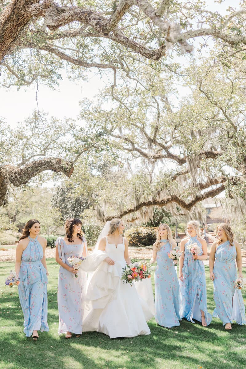 A bride walking with her bridesmaids beneath oak trees