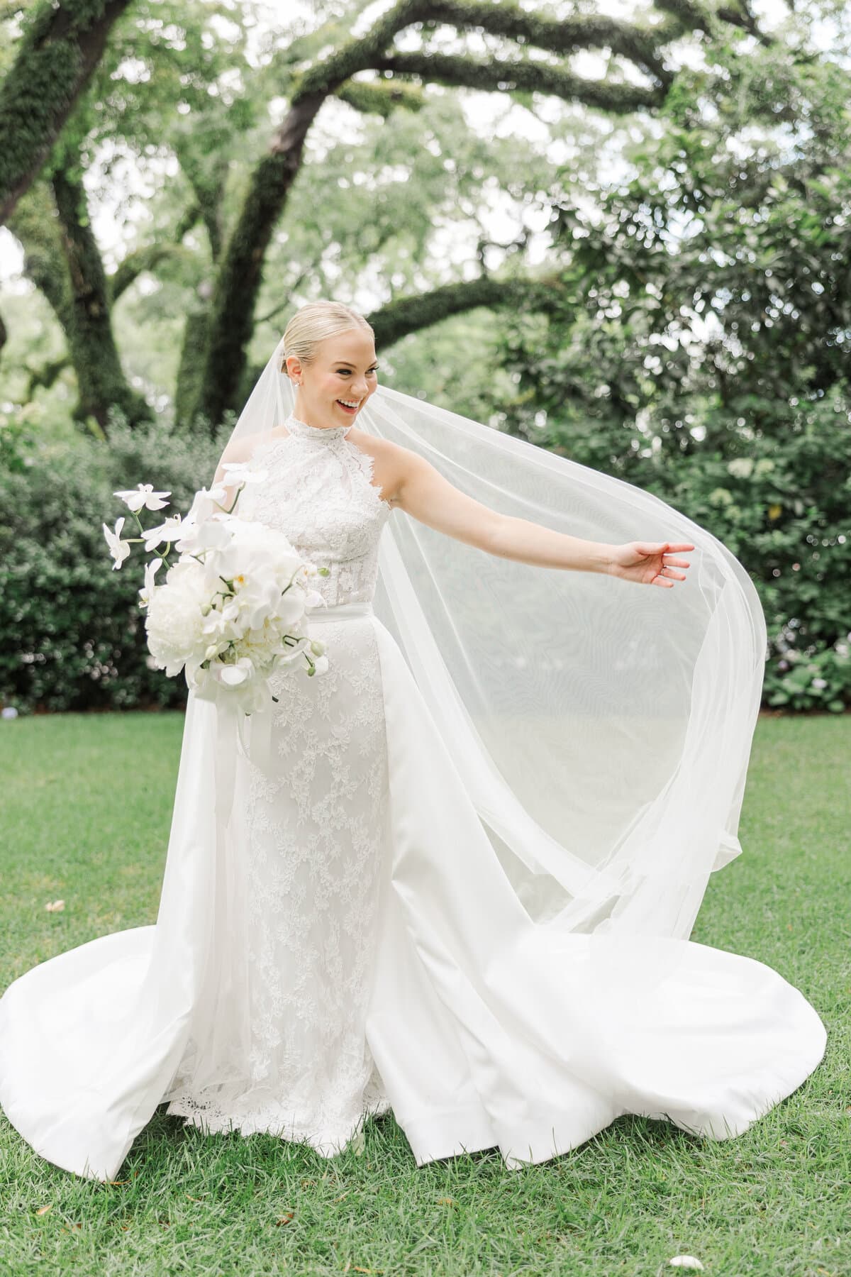 Bride lifting her veil beneath the oak trees