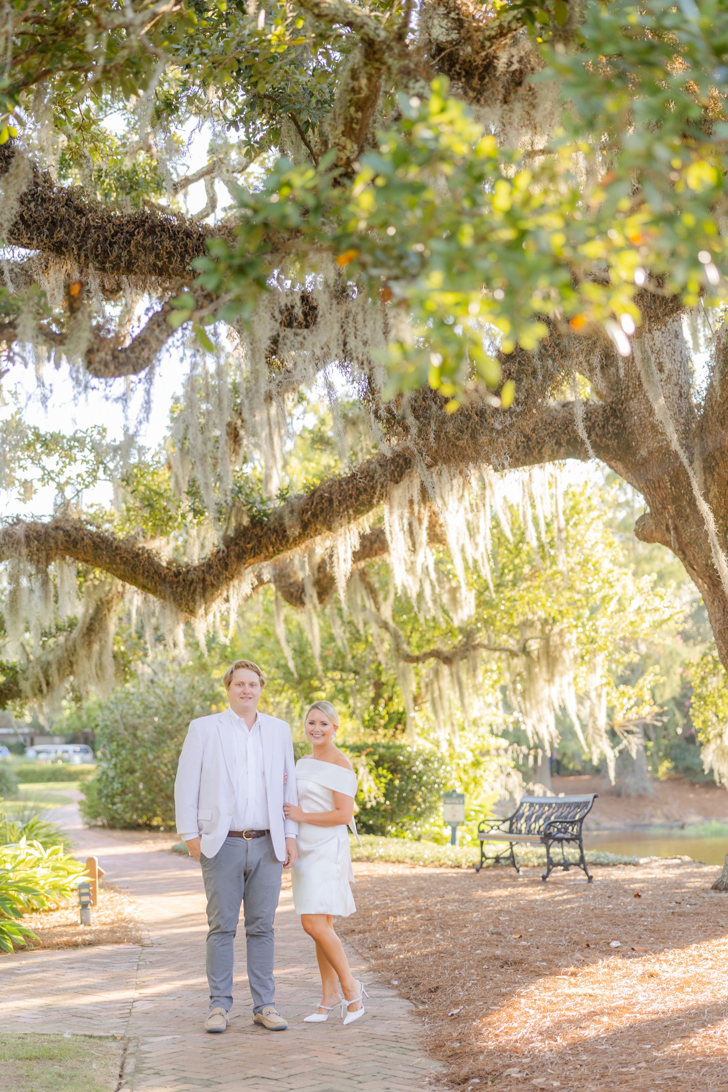 Romantic couple Audrey and Lyon, bathed in soft sunlight, share a loving moment beneath the mossy oak trees at the picturesque Grand Hotel in Fairhope.