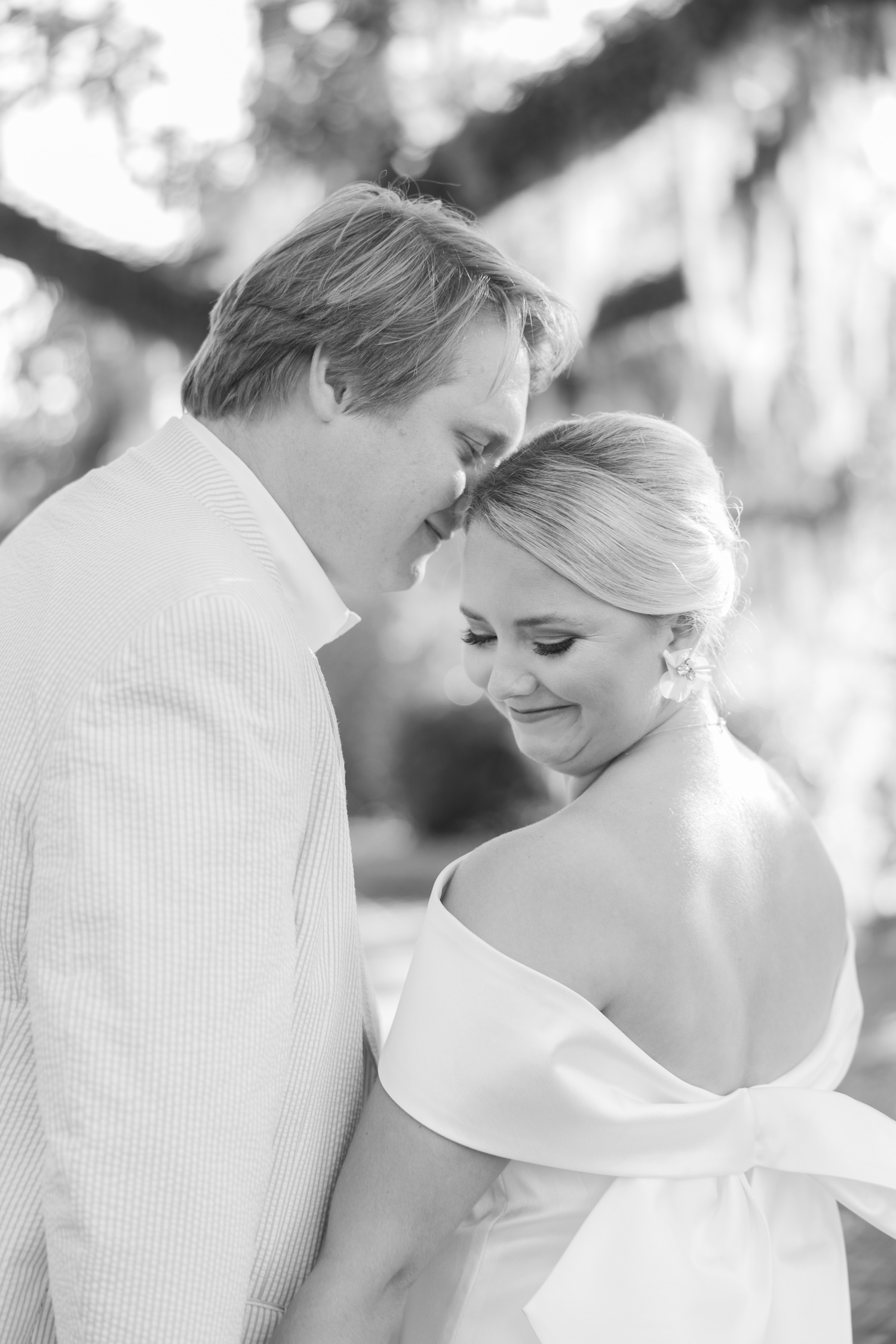 Romantic couple Audrey and Lyon, bathed in soft sunlight, share a loving moment beneath the mossy oak trees at the picturesque Grand Hotel in Fairhope.