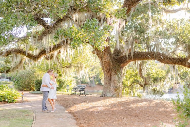 Romantic couple Audrey and Lyon, bathed in soft sunlight, share a loving moment beneath the mossy oak trees at the picturesque Grand Hotel in Fairhope.