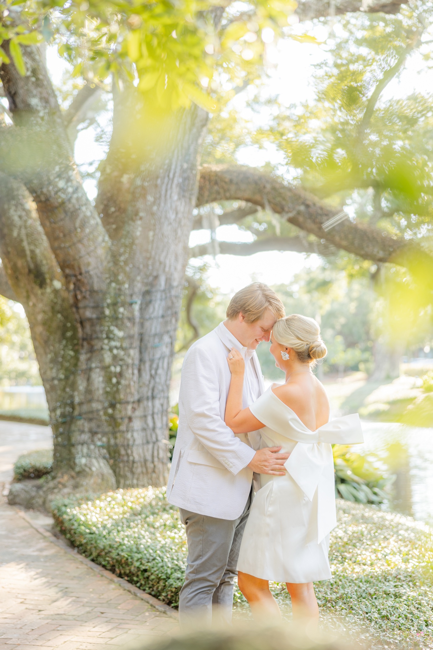 Romantic couple Audrey and Lyon, bathed in soft sunlight, share a loving moment beneath the mossy oak trees at the picturesque Grand Hotel in Fairhope.