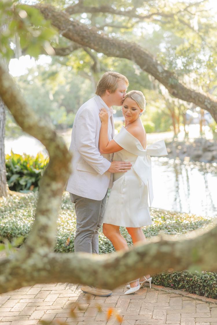 Romantic couple Audrey and Lyon, bathed in soft sunlight, share a loving moment beneath the mossy oak trees at the picturesque Grand Hotel in Fairhope.