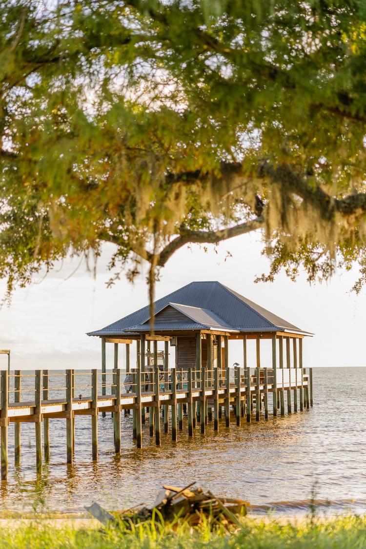 Romantic couple Audrey and Lyon, bathed in soft sunlight, share a loving moment beneath the mossy oak trees at the picturesque Grand Hotel in Fairhope.