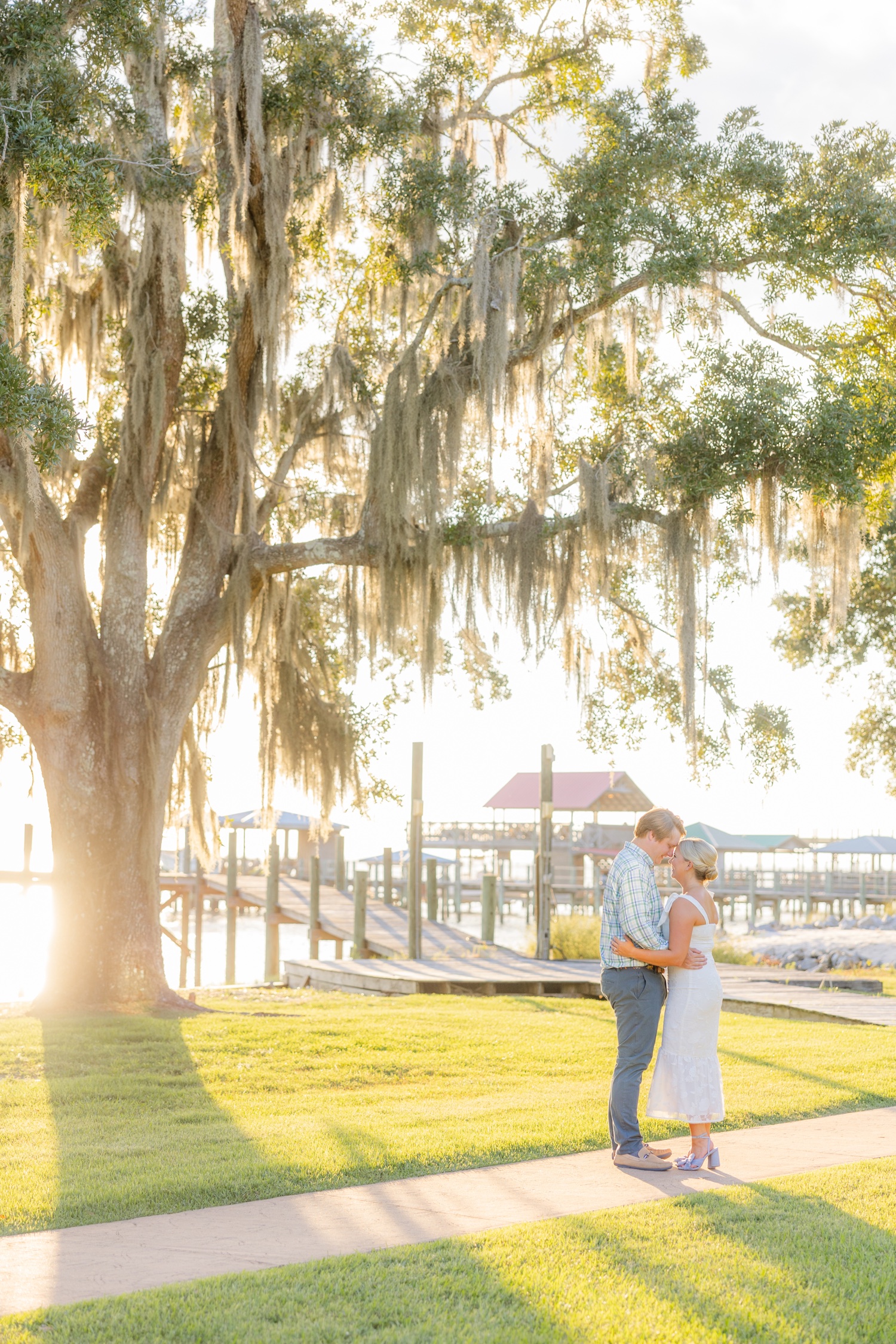 Romantic couple Audrey and Lyon, bathed in soft sunlight, share a loving moment beneath the mossy oak trees at the picturesque Grand Hotel in Fairhope.