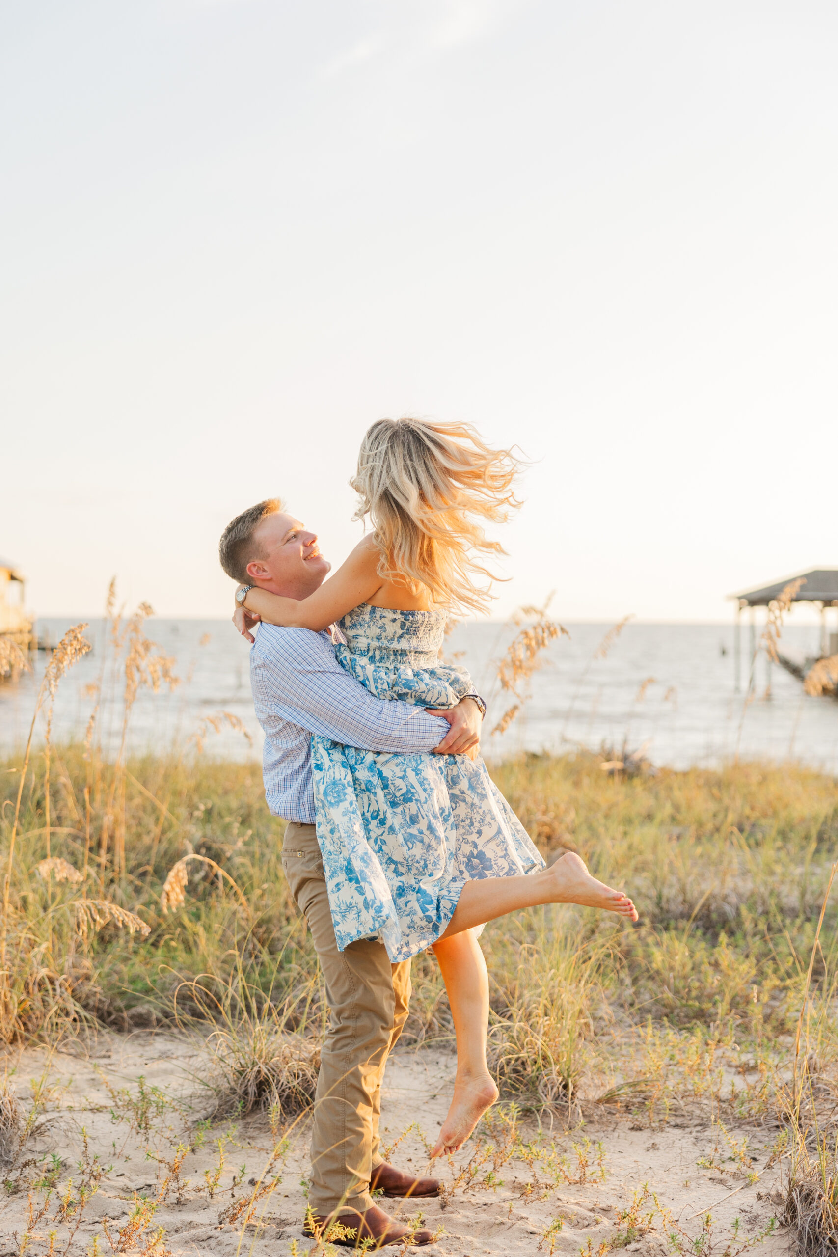 Groom-to-be lifts his fiancée in a joyful golden hour moment during their Point Clear, Alabama engagement session with Jennie Tewell Photography Let me know if you'd like these formatted for Pinterest too!