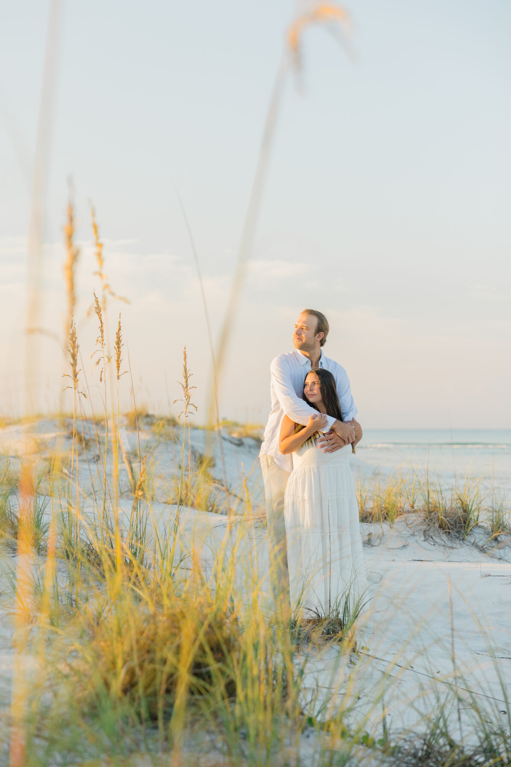 Engaged couple standing on the dunes at Grayton Beach during sunrise, with soft golden light and sea oats surrounding them | 30A engagement photographer